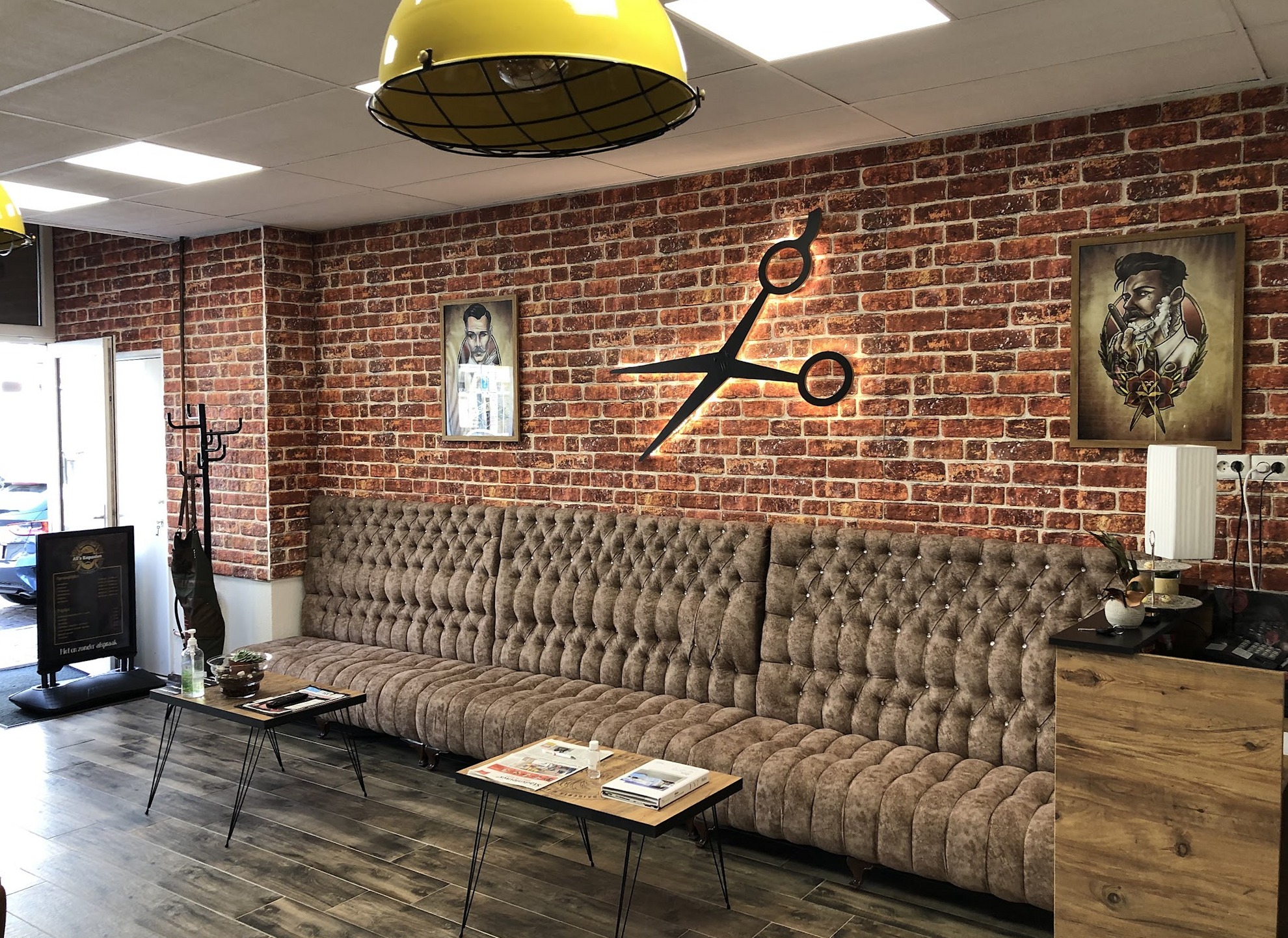 De wachthoek: een lange gecapitonneerde bank langs de bakstenen muur, met een gele lamp en salontafels